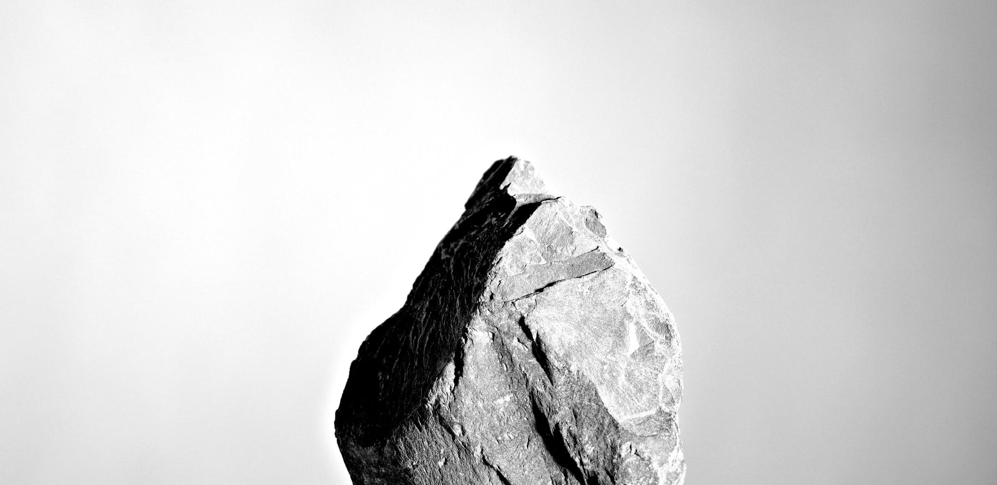 Black and white close up of a stone standing on it's thinnest point on a table, with a reflection in the table's surface